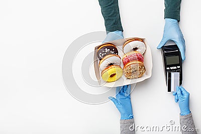 Fast food to go and order payment during covid pandemic. Waiter in rubber gloves gives box of colorful donuts, client Stock Photo