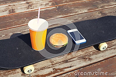 Fast food and unhealthy eating concept - juice cup, hamburger, smartphone on skateboard Stock Photo