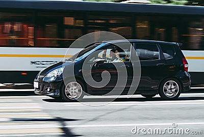 Fast moving black car on the city road. compact city hatchback with an old woman driving. Honda Jazz on the city street in motion Editorial Stock Photo