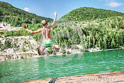 Fast running Boy jumping into mountain lake from the dock. Careless childhood concept image Stock Photo