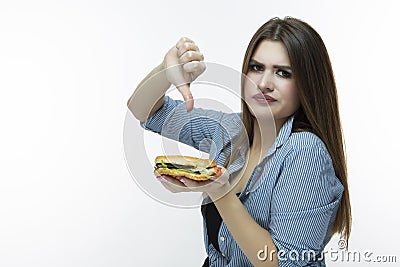 Fastfood Eating Concept. Young Caucasian Female Eating Burger And Thumbs Down Sign in Studio. Posing in Striped Shirt Indoors Stock Photo