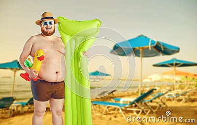 Fat funny man in swimming trunks with an inflatable mattress on a gray background. Stock Photo