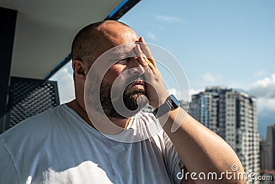 Fat man suffers dying from heat. Guy on balcony under hot summer sun sweats from high temperatures Stock Photo