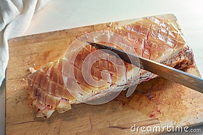 Fat rind of a piece of raw seasoned pork meat is incised with a kitchen knife on a cutting board, cooking preparation for a Stock Photo