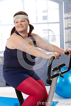 Fat woman on exercise bike Stock Photo