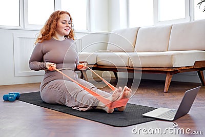 fat woman exercising with rubber bands according to online sports video on laptop Stock Photo