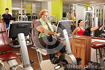 Fat woman training on exercise bike in gym Stock Photo