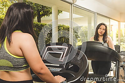 Fat Woman weight loss running on treadmill mirror reflect face smile happy to exercise in fitness gym Stock Photo
