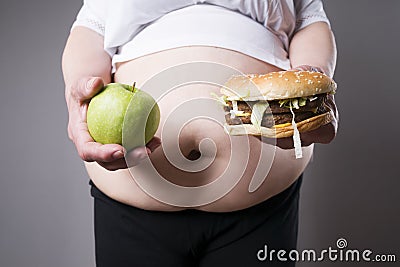 Fat women suffer from obesity with big hamburger and apple in hands, junk food concept Stock Photo