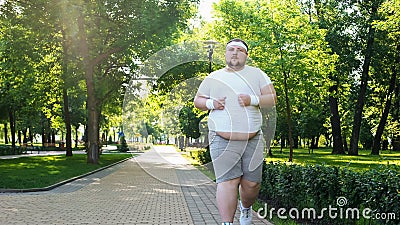 Fat young man jogging in park, obesity concept, struggling with insecurity Stock Photo