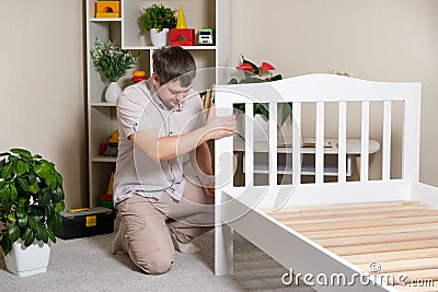 The father assembles the children& x27;s bed for the child, the man twists the screws into wooden furniture. Stock Photo