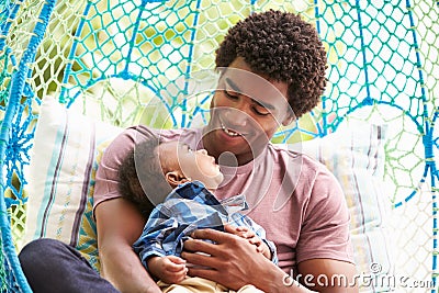 Father With Baby Son Relaxing On Outdoor Garden Swing Seat Stock Photo