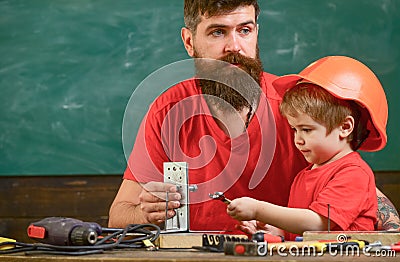 Father with beard teaching little son to use tools in classroom, chalkboard on background. Mens work concept. Boy, child Stock Photo