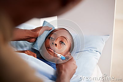 Father Caring For Sick Son Ill In Bed Taking Temperature With Thermometer Stock Photo