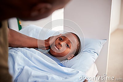 Father Caring For Sick Son Lying Ill In Bed At Home Stock Photo