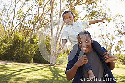 Father Carrying Son On Shoulders As They Walk In Park Stock Photo