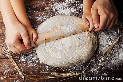 Father and child hands making the dough with flour, rolling pin and wheat ears on rustic wooden table top view. Stock Photo