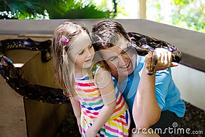 Father and child hold and feed python snake at zoo Stock Photo