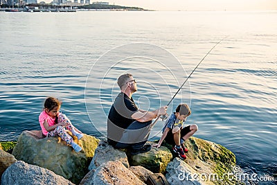 Father with children on a fishing trip by the sea. A boy and a girl with their father have fun fishing on the beach or by the sea. Stock Photo