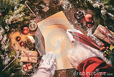 Father Christmas writing a seasonal letter using a vintage feather quill pen on old yellowed paper surrounded by Xmas decorations Stock Photo