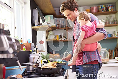 Father Cooking Meal Whilst Holding Daughter In Kitchen Stock Photo