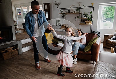 Father and daughter dance happily together while mother sits comfortably on living room sofa Stock Photo