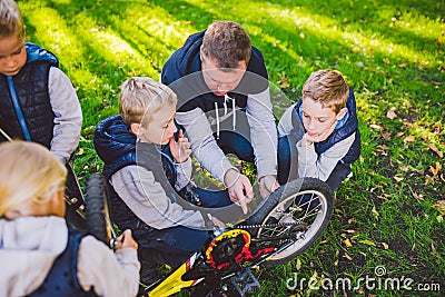 Father day. A large friendly family father and sons together actively relax in the fresh air. Dad teaches sons to repair bicycles Stock Photo