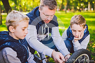 Father day. A large friendly family father and sons together actively relax in the fresh air. Dad teaches sons to repair bicycles Stock Photo