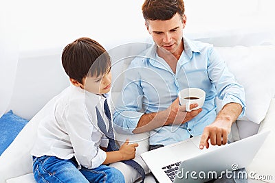 Father drinking coffee and teaching son how to use notebook. Stock Photo