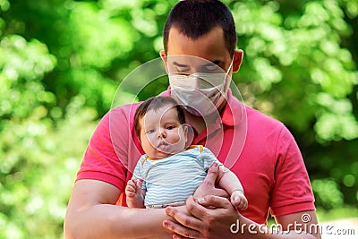 Father in facial mask holding in arms little baby daughter in summer day. Green leaves in background. Parenting during quarantine Stock Photo