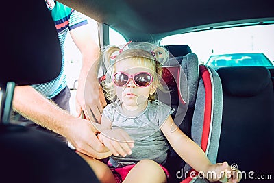 Father fasten blondy baby daughter 2-3 year old in car seat standing on parking. Transport, safety, childhood road trip and people Stock Photo