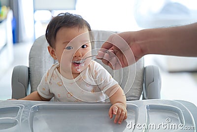 Asian father giving porridge to his kid on baby feeding seat. Stock Photo