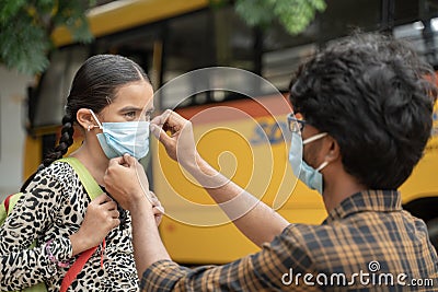 Father helping daughter to wear mask before getting inside the school bus as coronavirus or covid-19 safety measures - concept of Stock Photo