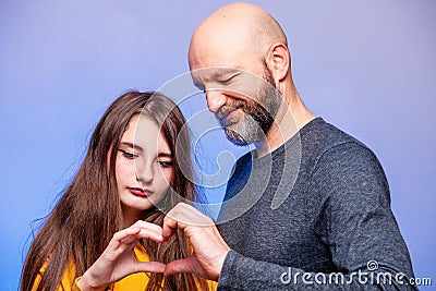 Father and his daughter interactions. Models man in his 40s, bald with grey beard. girl teenager with long hair. Making heart. Stock Photo