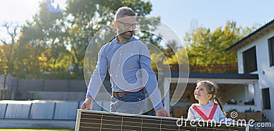 Father with his little daughter carring solar panel at their backyard. Alternative energy, saving resources and Stock Photo