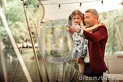 Father holding his daughter while looking at ducks in lake Stock Photo