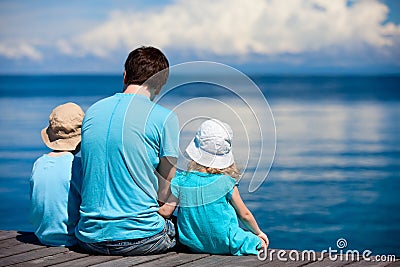 Father and kids sitting on wooden dock Stock Photo