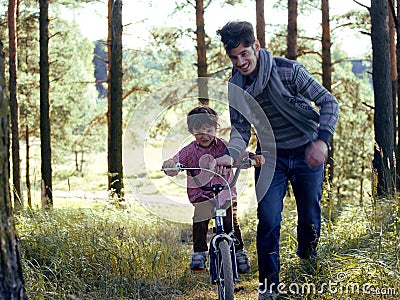 Father learning his son to ride on bicycle outside, real happy family in summer forest enjoing nature Stock Photo