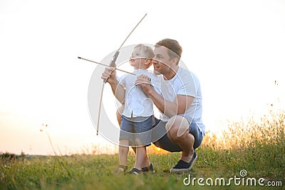 Father is learning his son to shoot from bow in sunny summer day. Stock Photo