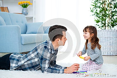 Father and little daughter having quality family time together at home. dad with girl lying on warm floor drawing with colorful Stock Photo