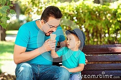 Father and little son eating ice-cream together in park in sunny summer or autumn day. Boy offers ice-cream to daddy. Happy family Stock Photo