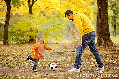 Dad and son having fun outdoors: little boy playing soccer with father in autumn park Stock Photo