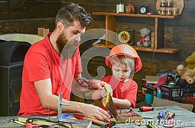 Father, parent with beard teaching little son to sawing with sharp handsaw, carpenter crafts. Masculine duties concept Stock Photo