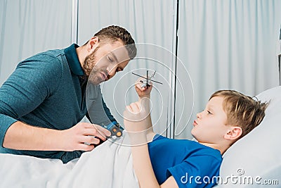 Father playing with sick little boy lying in hospital bed, dad and son in hospital Stock Photo