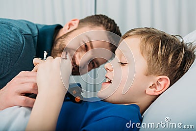 Father playing with sick little boy lying in hospital bed, dad and son in hospital Stock Photo