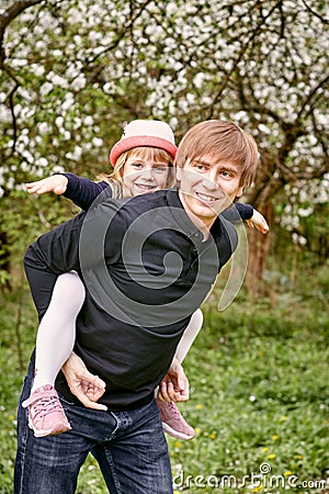 Father plays with his daughter in a flowering garden. Against the background of green grass and flowering trees Stock Photo