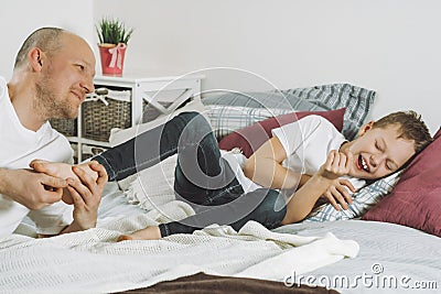 Father plays with his son 7-10 on bed. Dad tickles kids feet. Family, having fun Stock Photo
