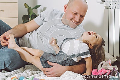 Father plays with little daughter 2-4 on floor. Dad tickles kids feet. Family having fun Stock Photo