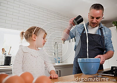 Father pouring ingredients into bowel baking with daughter in organised kitchen. Stock Photo