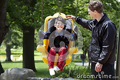 Father pushing disabled boy in special needs swing Stock Photo